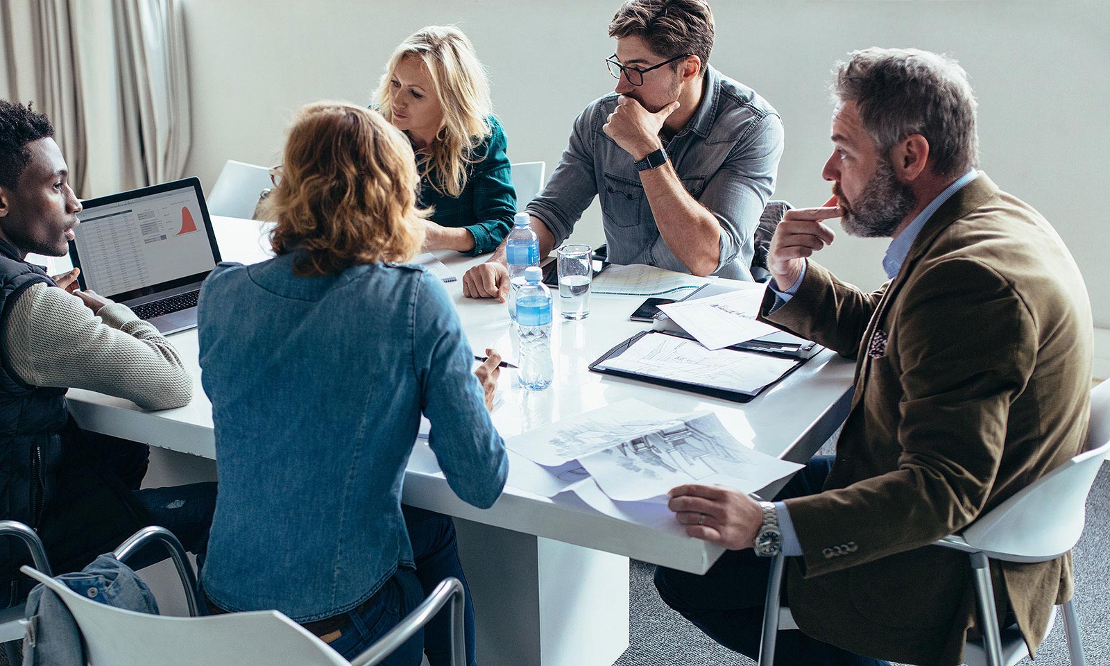 Fem personer har et møte om Grow Your Business. De sitter rundt et bord med papirer og en datamaskin foran seg. Alle ser engasjerte ut mens de diskuterer.